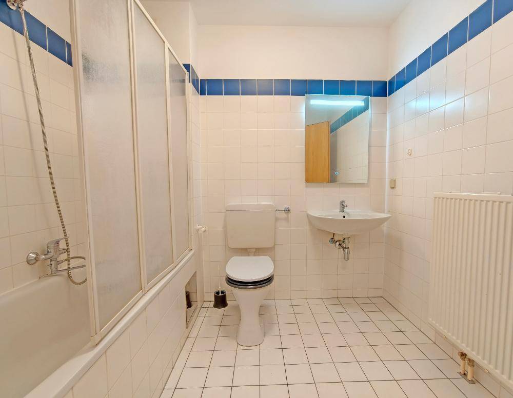 Gefliestes Badezimmer mit Badewanne, WC, Waschbecken und blauen Akzentstreifen, in gutem Zustand.
