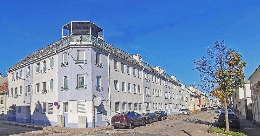 Mehrstöckiges Wohngebäude mit Dachterrasse und geparkten Autos an einer städtischen Straße.