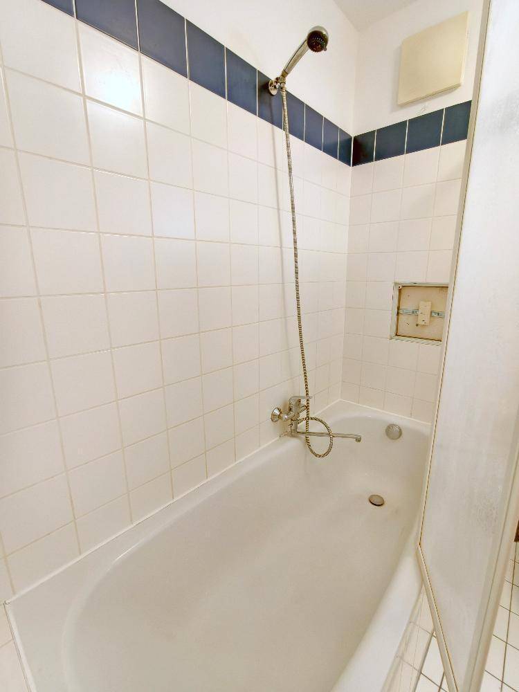Badewanne mit Duschvorrichtung und weißen Fliesen, akzentuiert durch einen blauen Streifen, sauber und funktional.