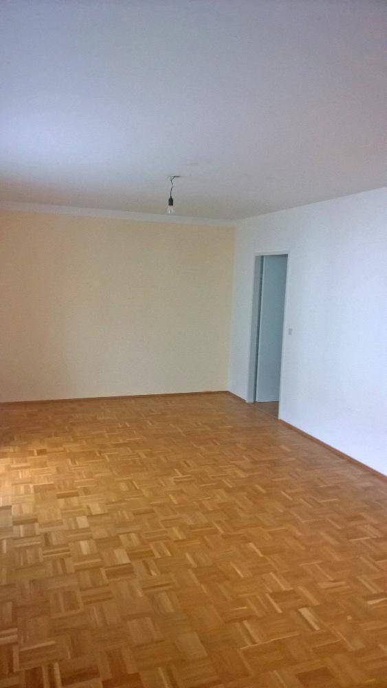 Geräumiges, leeres Zimmer mit Fischgrätparkettboden und hellen Wänden, bereit zur Einrichtung.