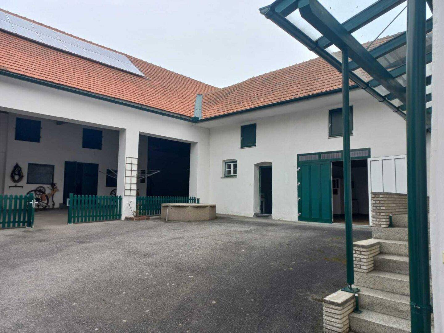Geräumiger Innenhof mit mehreren Gebäuden, einem Brunnen und Solarpaneelen auf dem Dach.