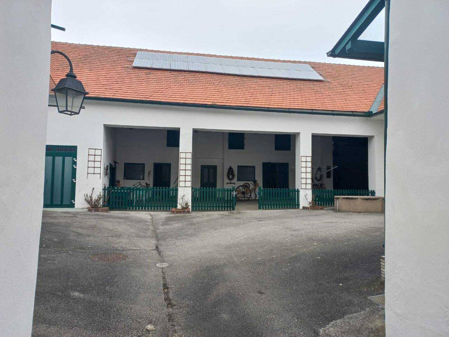 Weitläufiger Innenhof mit mehreren Gebäuden, grünen Zäunen und Solarpaneelen auf dem Dach.