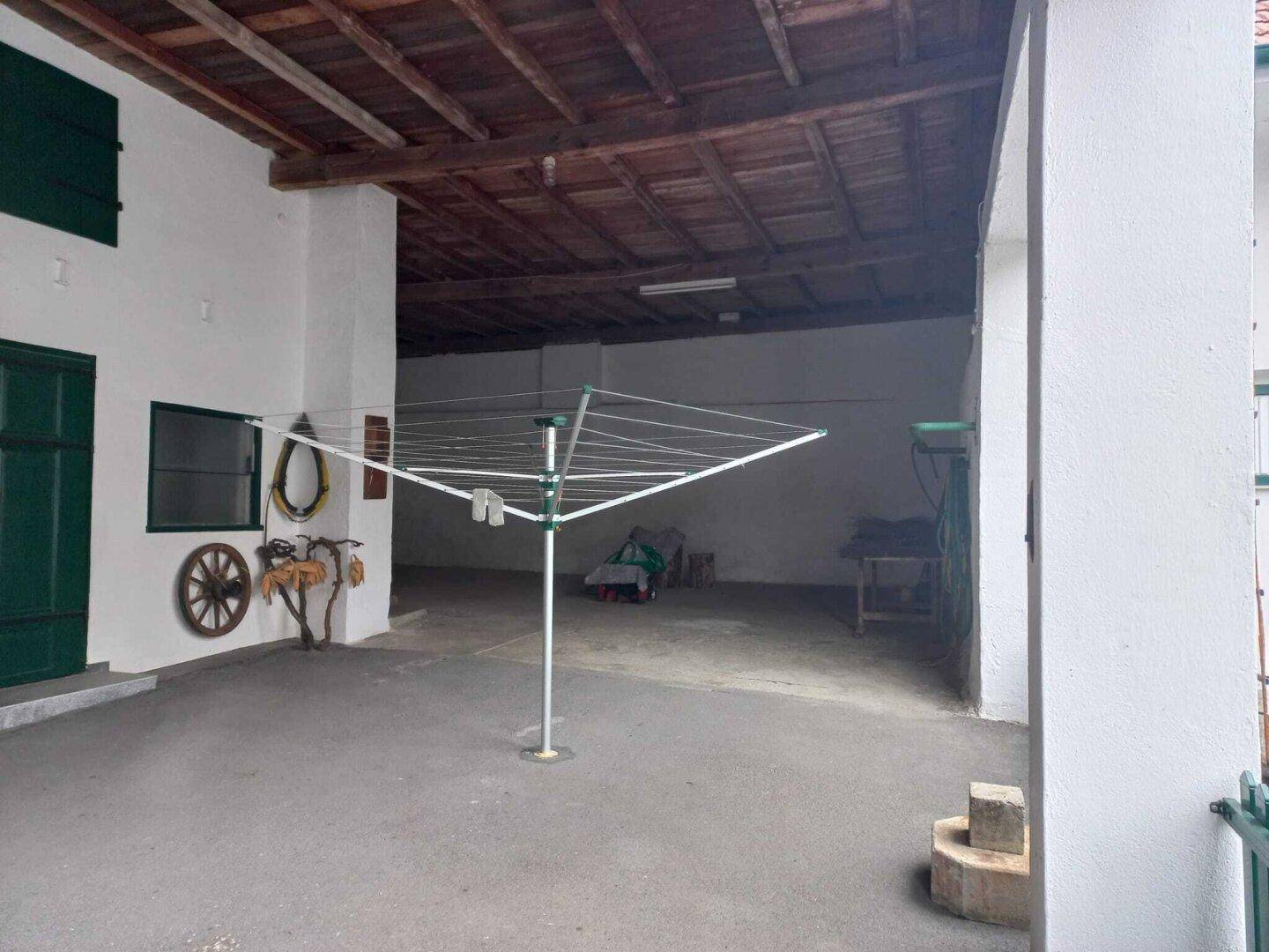 Überdachter Außenbereich mit Wäscheständer und Holzbalkendecke, ideal für Lagerung oder Parken.