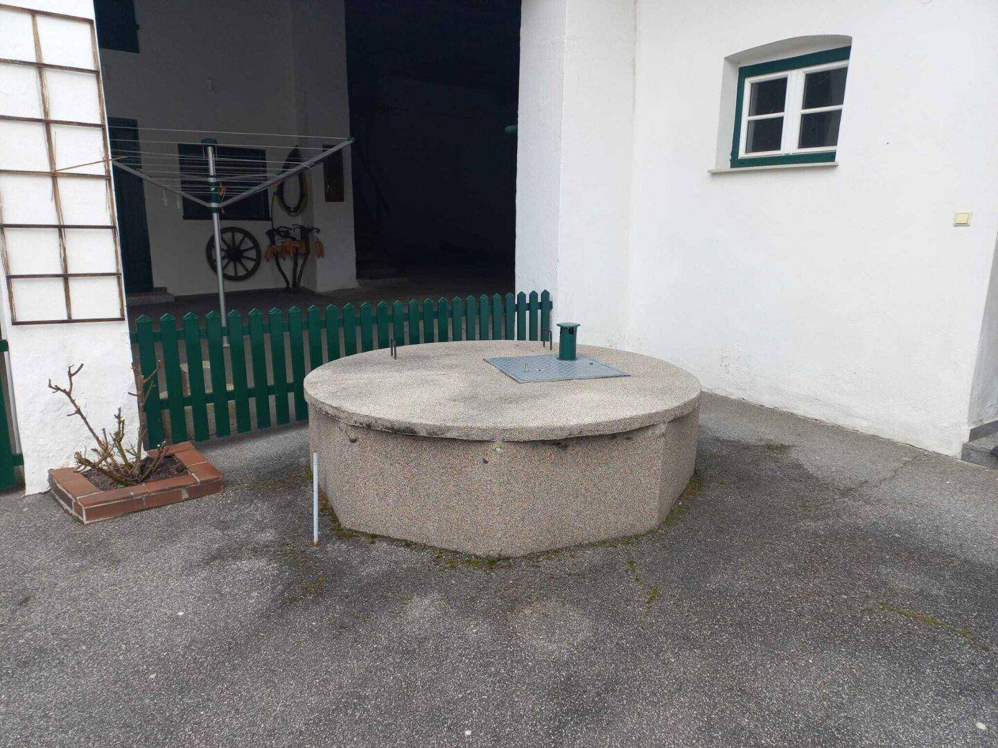 Detailansicht eines runden Brunnens im gepflasterten Innenhof, umgeben von Grün.