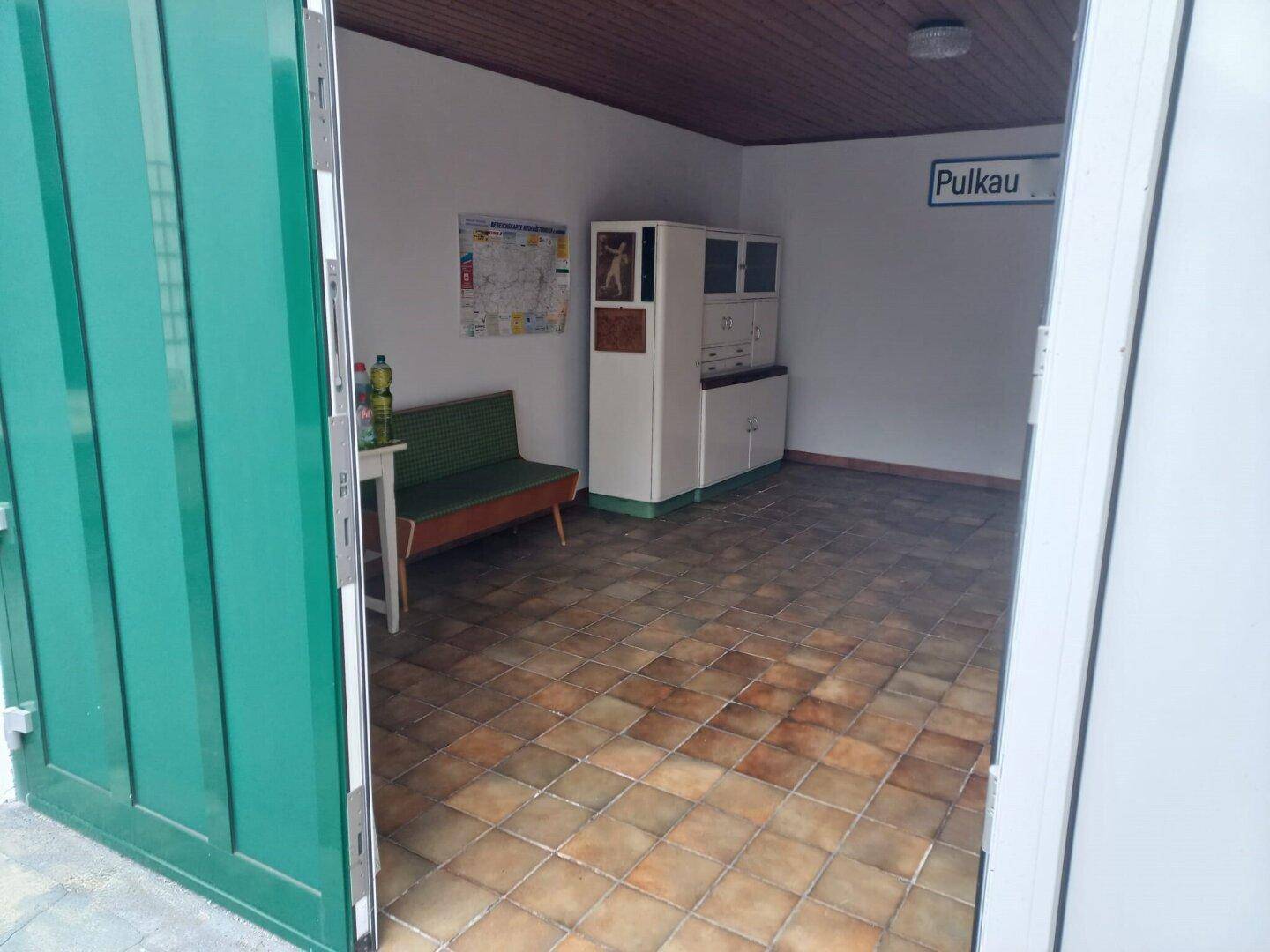 Einfacher Raum mit Fliesenboden, einer Bank und einem Schrank, möglicherweise ein Wartebereich.
