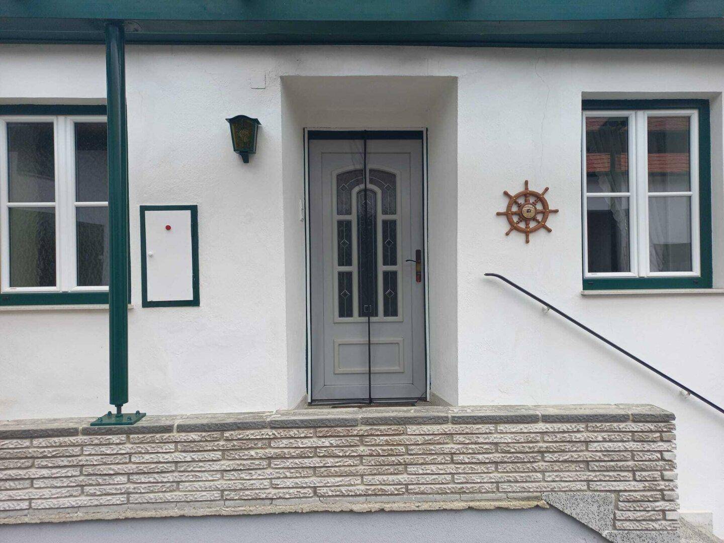 Detailansicht der Haustür mit dekorativen Glaseinsätzen und einem Steuerrad als Dekoration.
