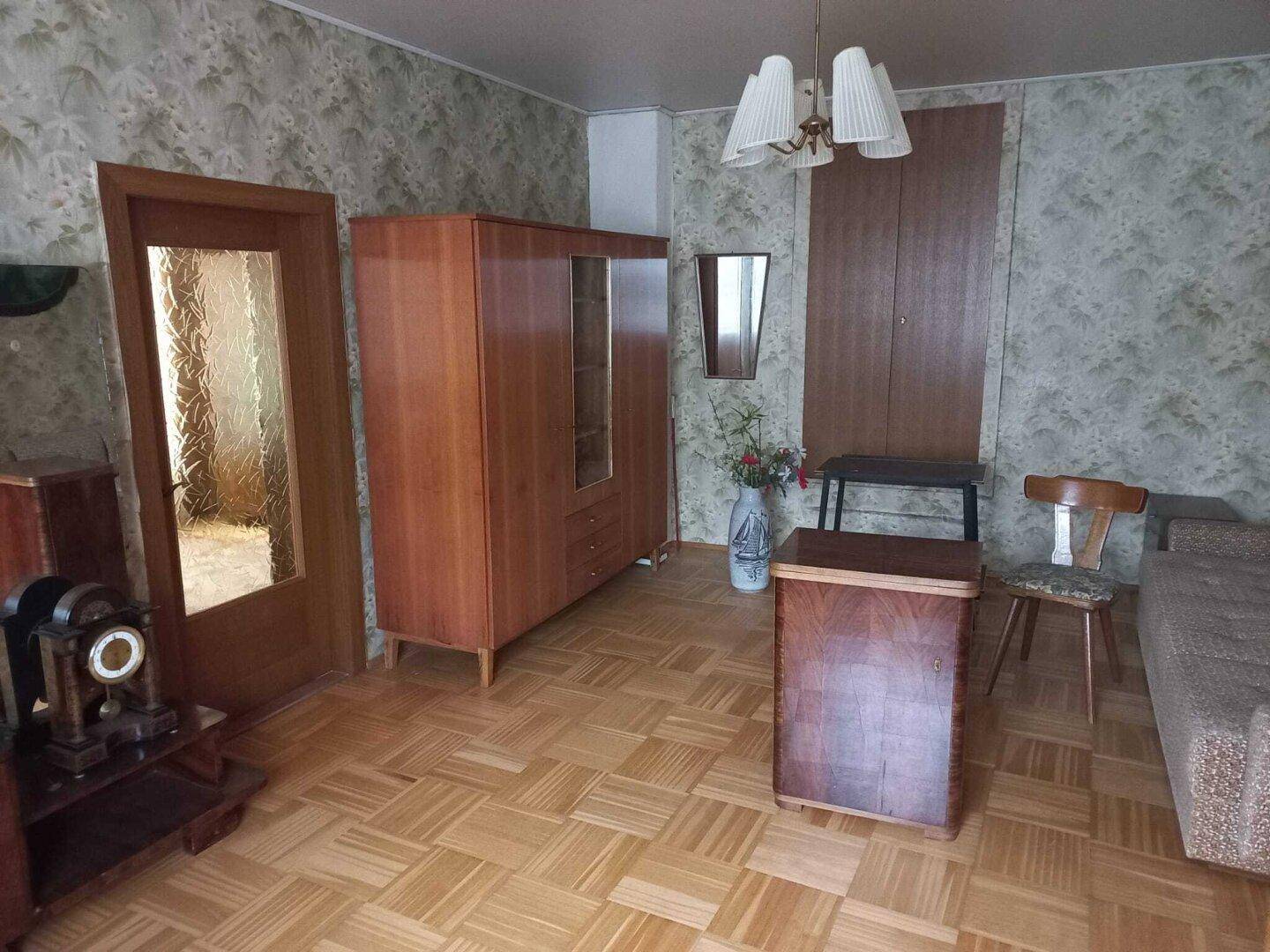Wohnzimmer mit Fischgrätparkett, gemusterter Tapete und traditionellen Holzmöbeln.