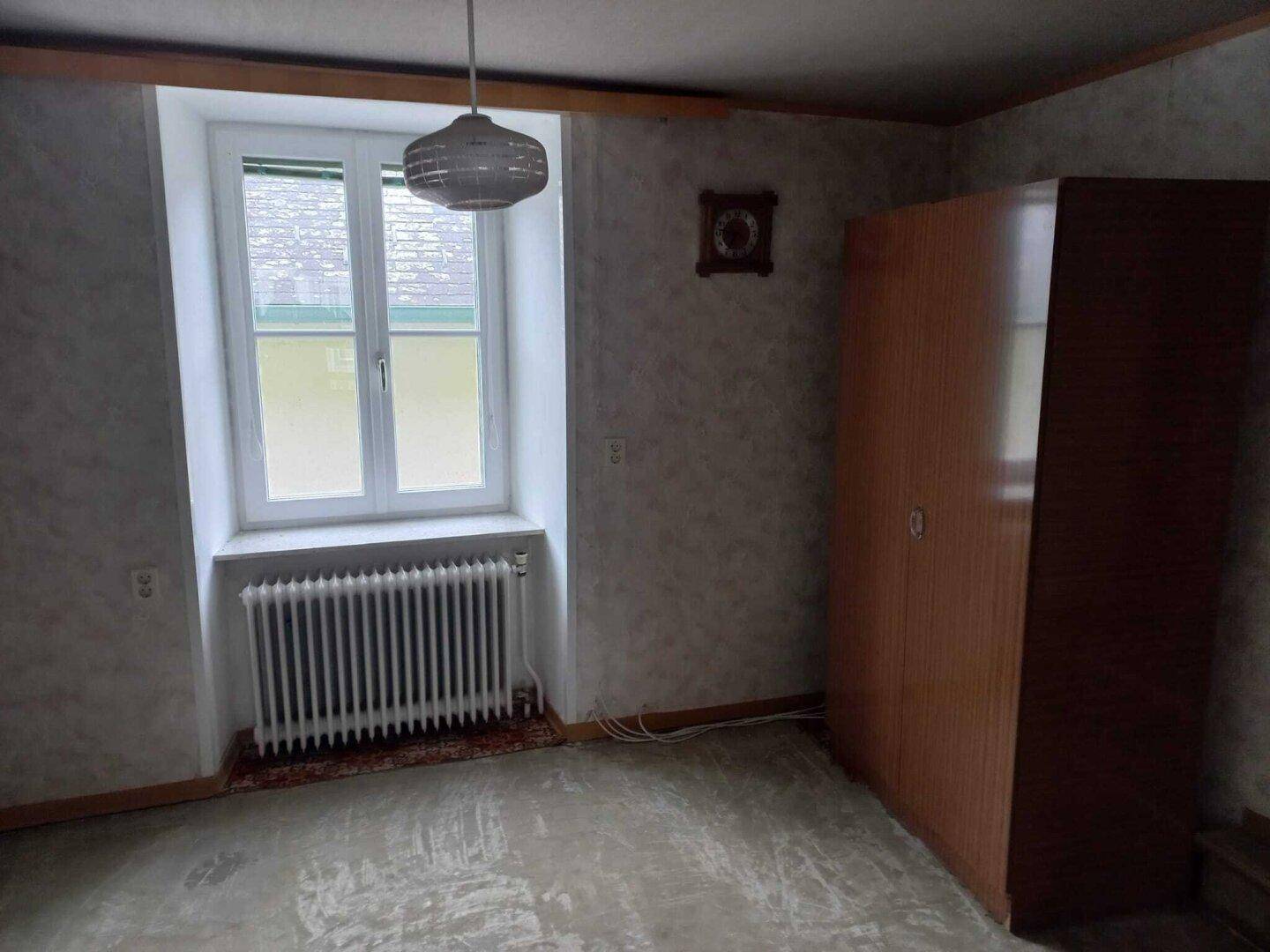 Schlafzimmer mit Fenster, Heizkörper und einem Kleiderschrank, bereit zur individuellen Gestaltung.