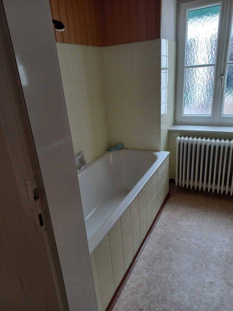 Badezimmer mit Badewanne, gelben Fliesen und einem Fenster, das Tageslicht hereinlässt.