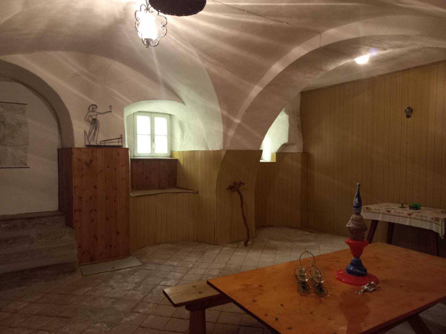 Historischer Kellerraum mit gewölbter Decke, Holzvertäfelung und rustikalem Mobiliar.