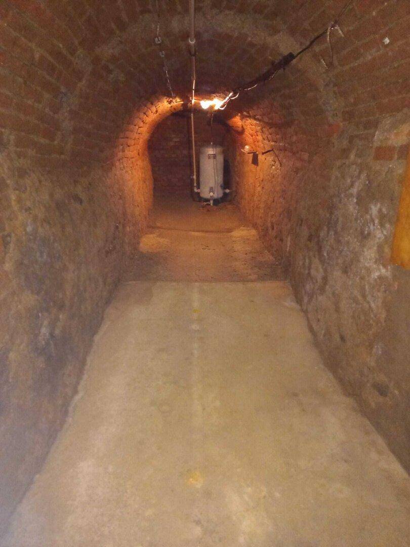 Langer, schmaler Kellergang mit Ziegelwänden und gewölbter Decke, der in die Tiefe führt.