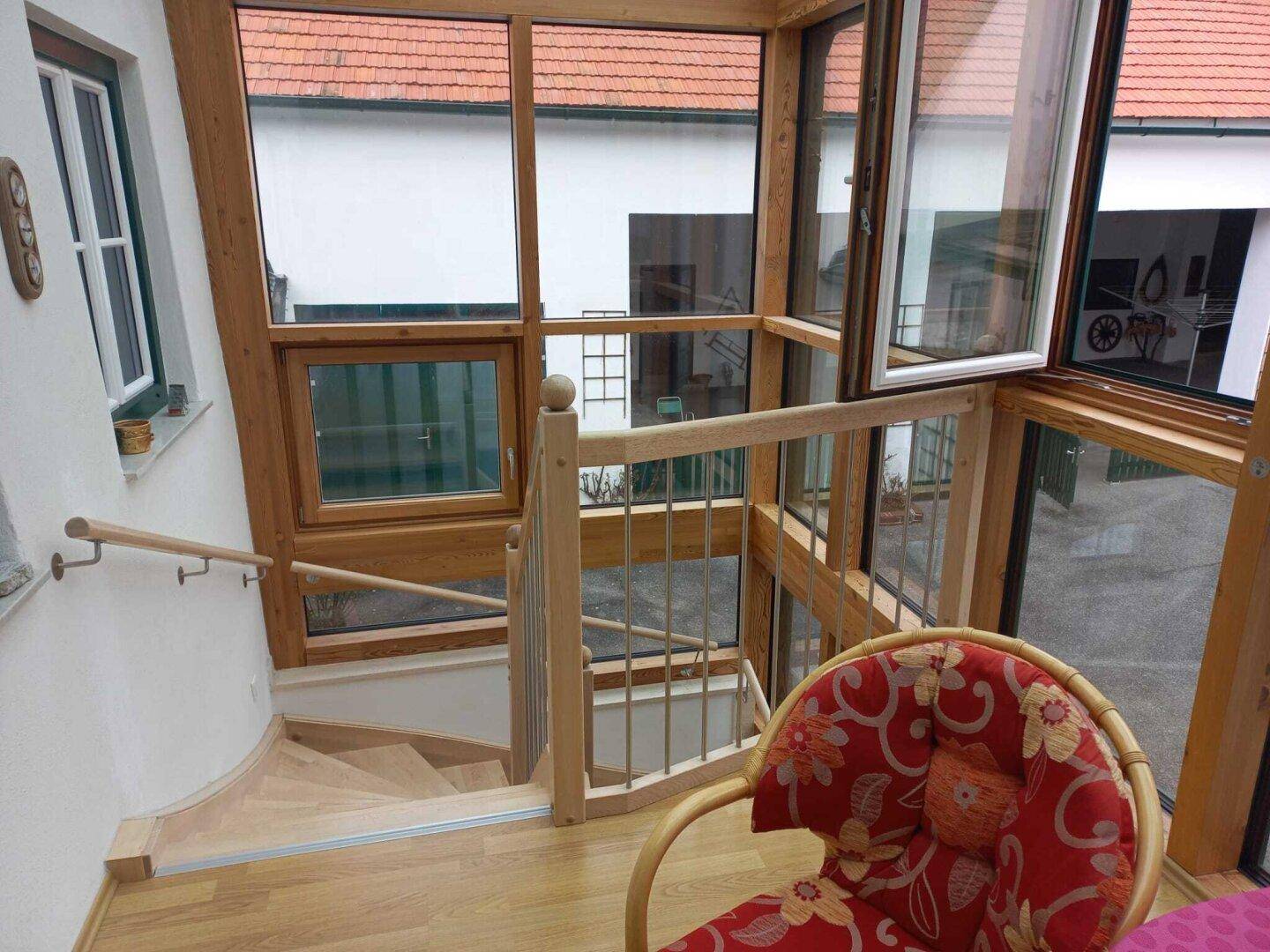 Heller Wintergarten mit Holzrahmenfenstern, Treppe und Blick auf den Innenhof.