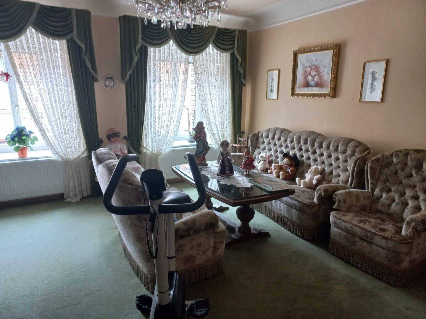 Klassisches Wohnzimmer mit plüschigen Sofas, Kronleuchter und Heimtrainer.