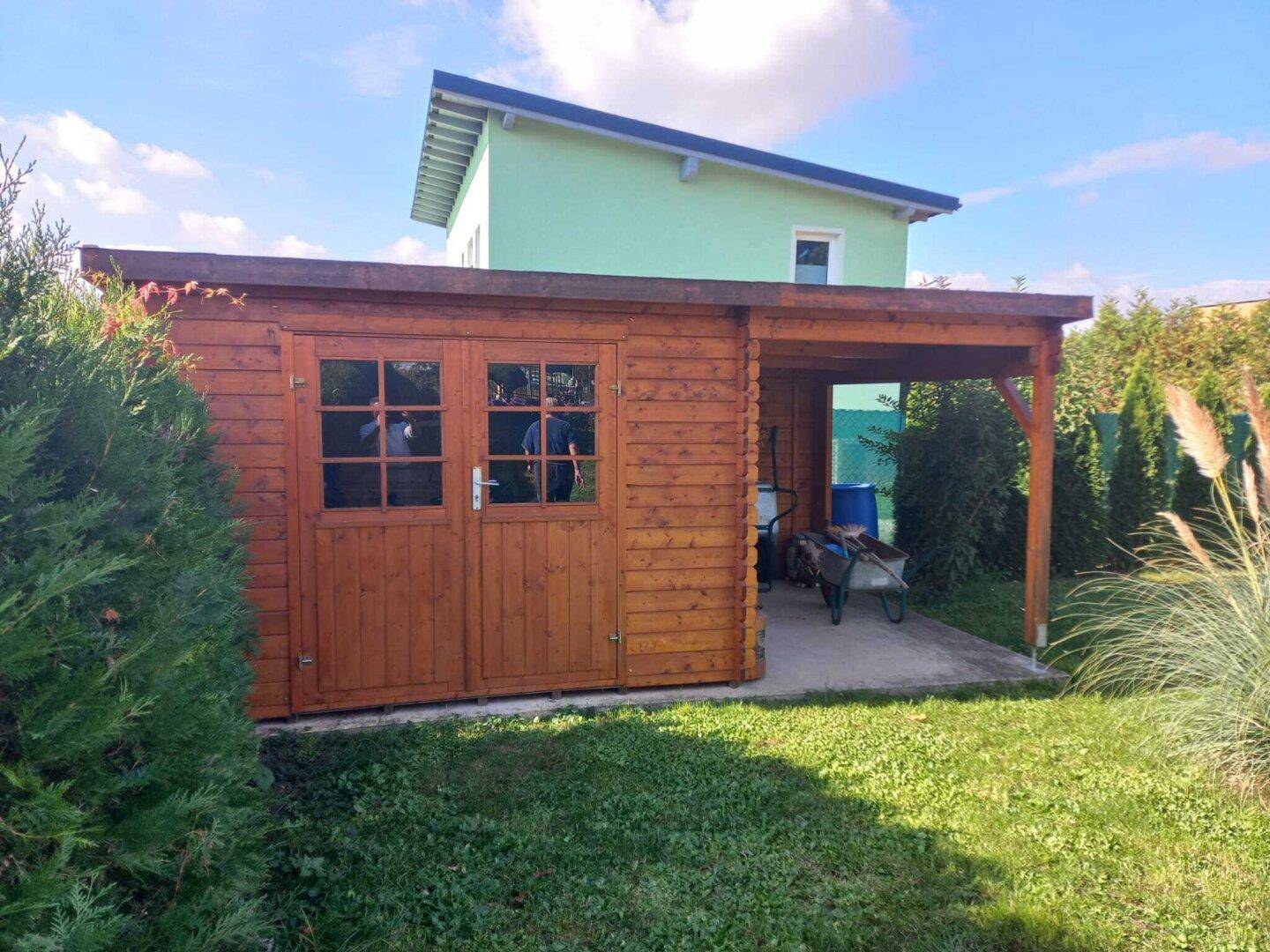 Geräumiges Gartenhaus aus Holz mit einem überdachten Bereich, umgeben von Grünflächen.