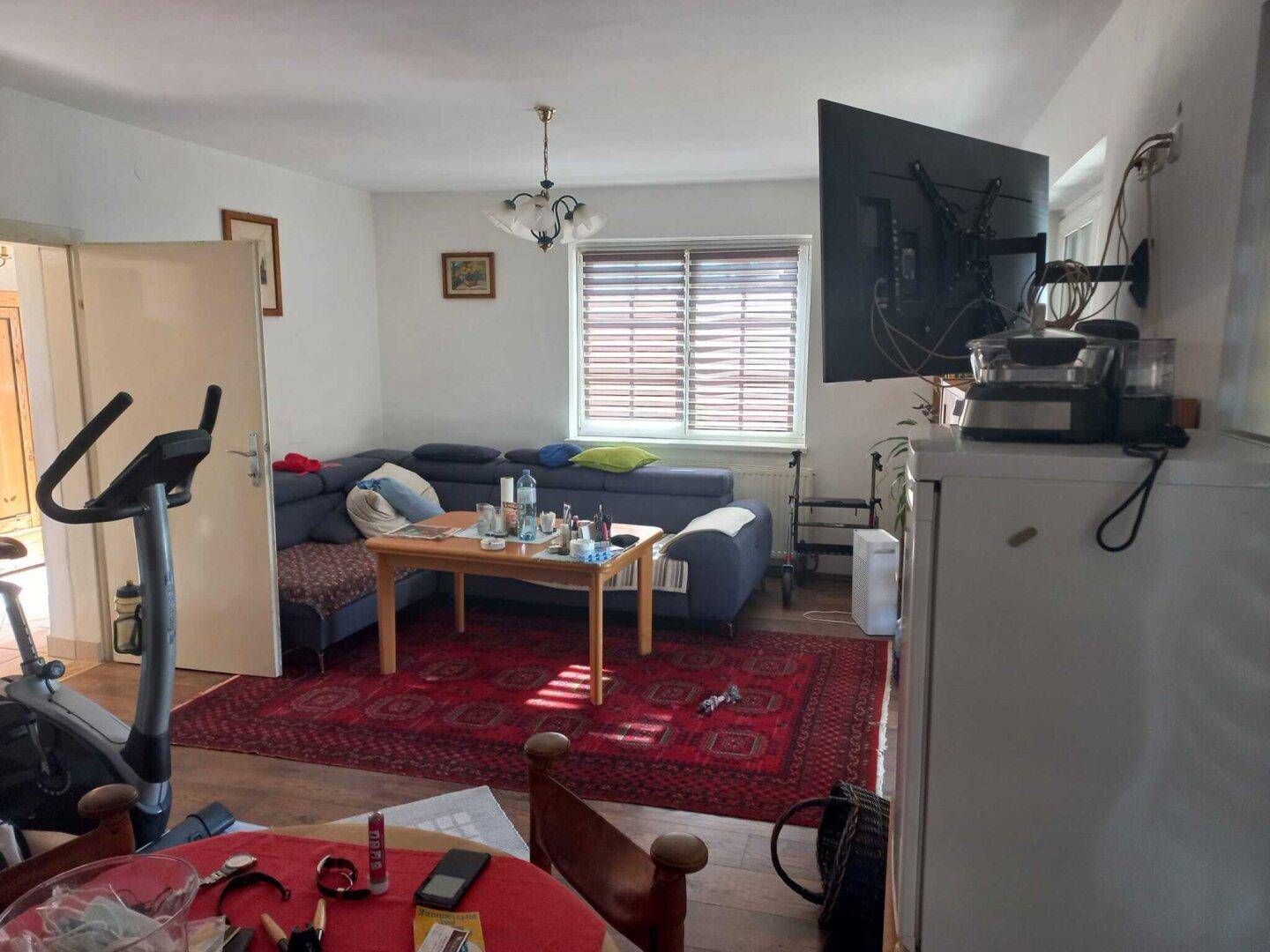 Geräumiges Wohnzimmer mit blauem Ecksofa, Couchtisch und großem Wandfernseher.
