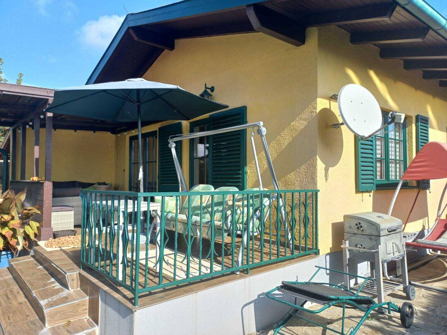 Gemütliche Terrasse mit Gartenmöbeln, Sonnenschirm und Grill, ideal für entspannte Stunden im Freien.