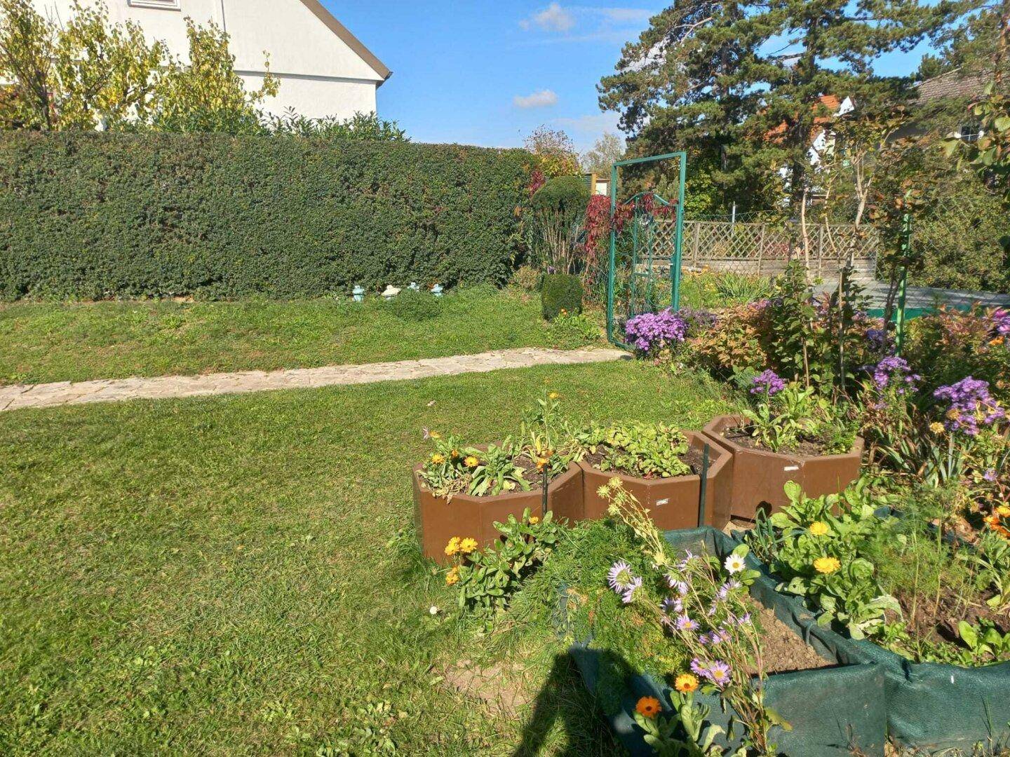 Gartenbereich mit Hochbeeten für Pflanzen und einem dekorativen grünen Gartentor.