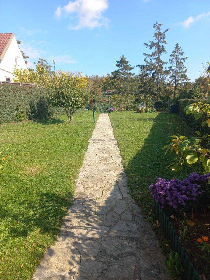 Langer Steinweg führt durch den gepflegten grünen Garten mit Bäumen und Hecken.