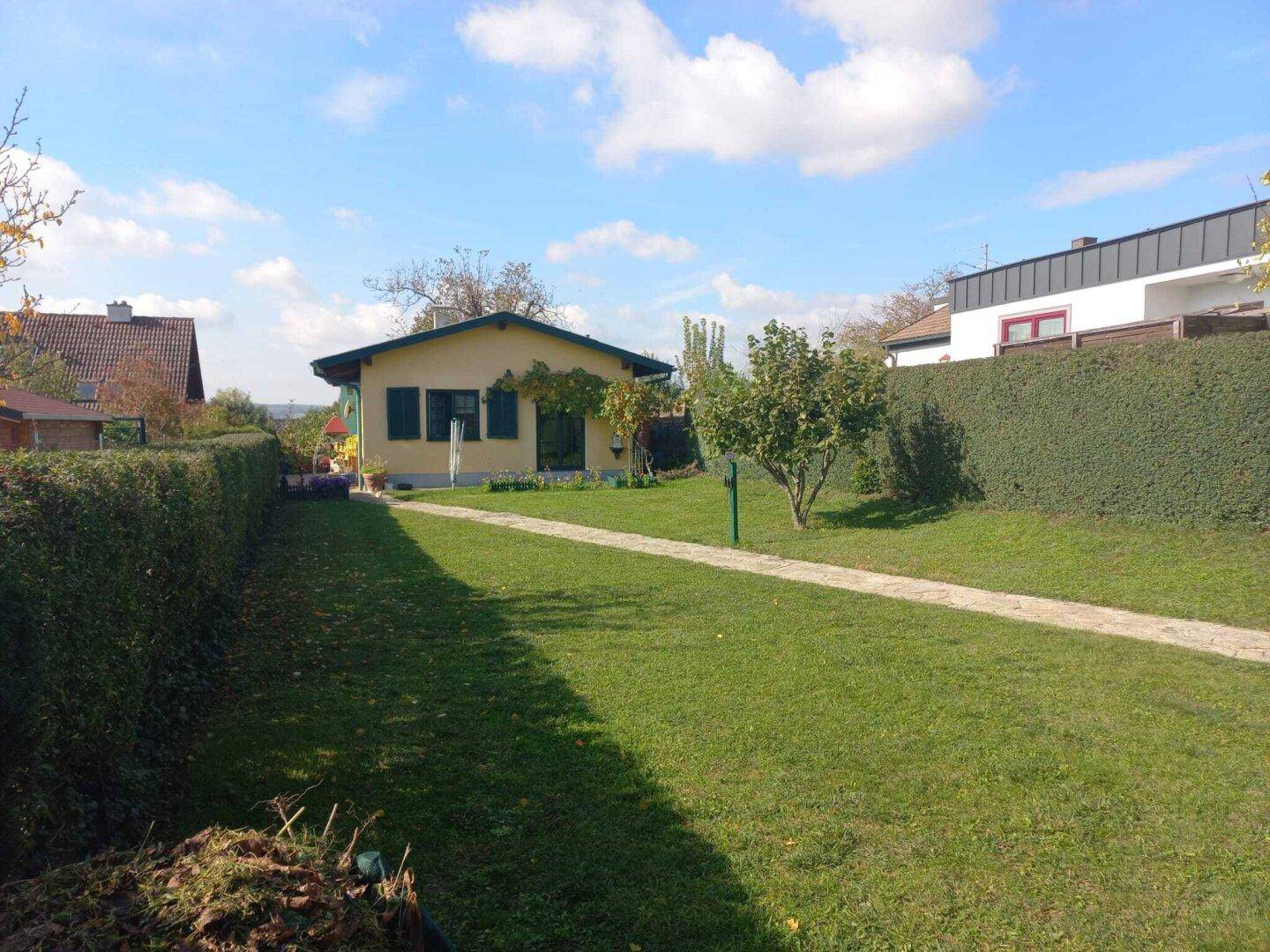 Weitläufiger Garten mit Rasenfläche, Steinweg und dem Haus im Hintergrund, umgeben von Hecken.