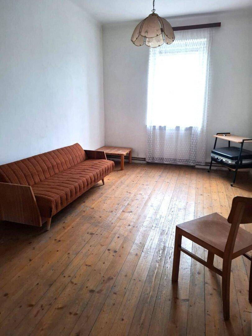 Helles Wohnzimmer mit Holzdielenboden, einem Vintage-Sofa und einem Fenster mit hellen Vorhängen.