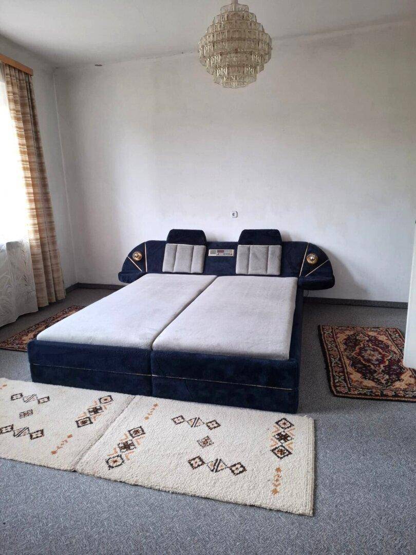Schlafzimmer mit einem großen Doppelbett, Teppichboden und einem auffälligen Kronleuchter an der Decke.