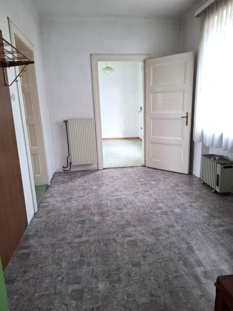 Flur mit gemustertem Vinylboden, Heizkörper und einer offenen Tür, die in einen weiteren Raum führt.