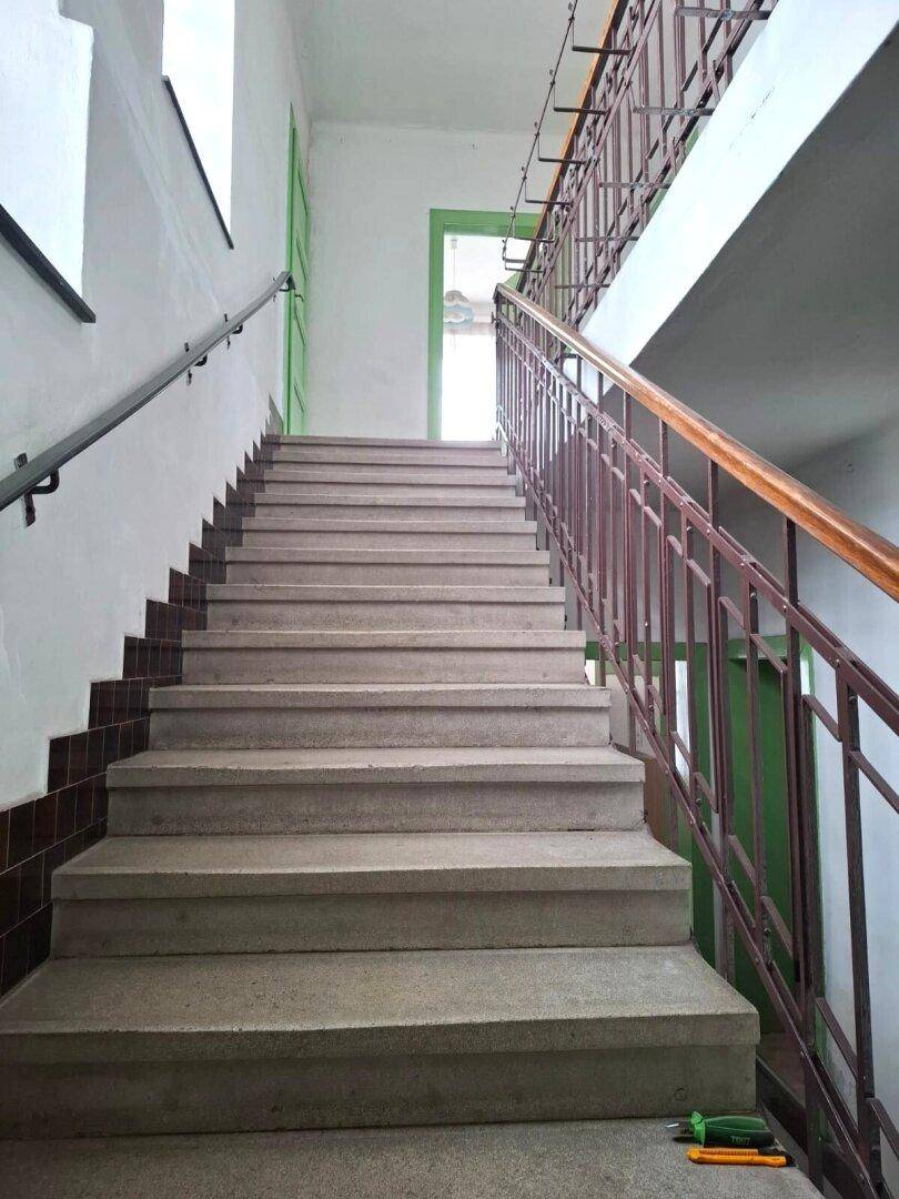 Treppenhaus mit Steinstufen, einem robusten Metallgeländer und einem Handlauf aus Holz.