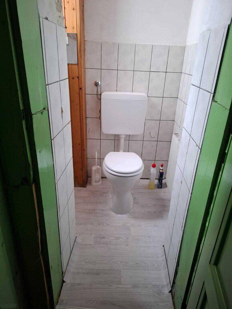 Schlichtes WC mit weißen Fliesen an den Wänden und einem hellen Vinylboden in Holzoptik.