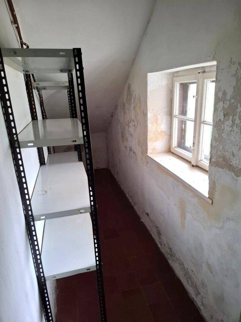Abstellraum im Dachgeschoss mit Regalen, einem kleinen Fenster und sichtbaren Abnutzungsspuren an den Wänden.