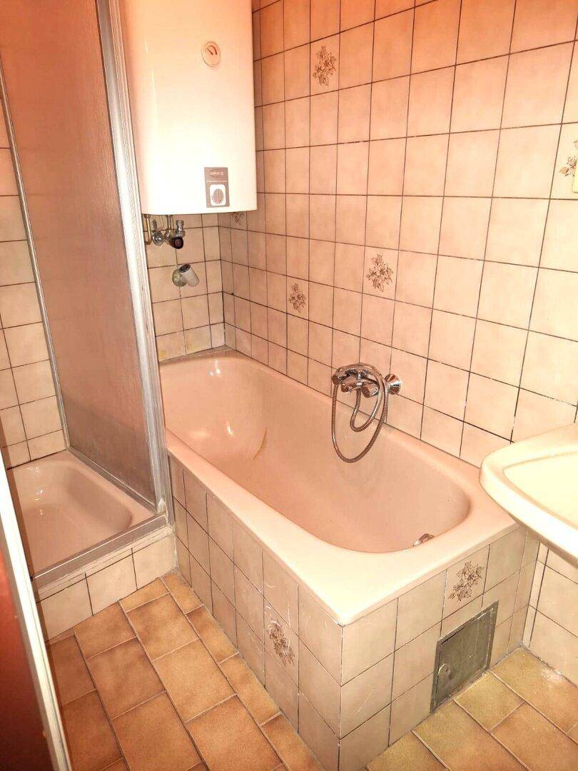 Badezimmer mit Badewanne, Duschkabine, Waschbecken und beigefarbenen Fliesen im 80er-Jahre-Stil.