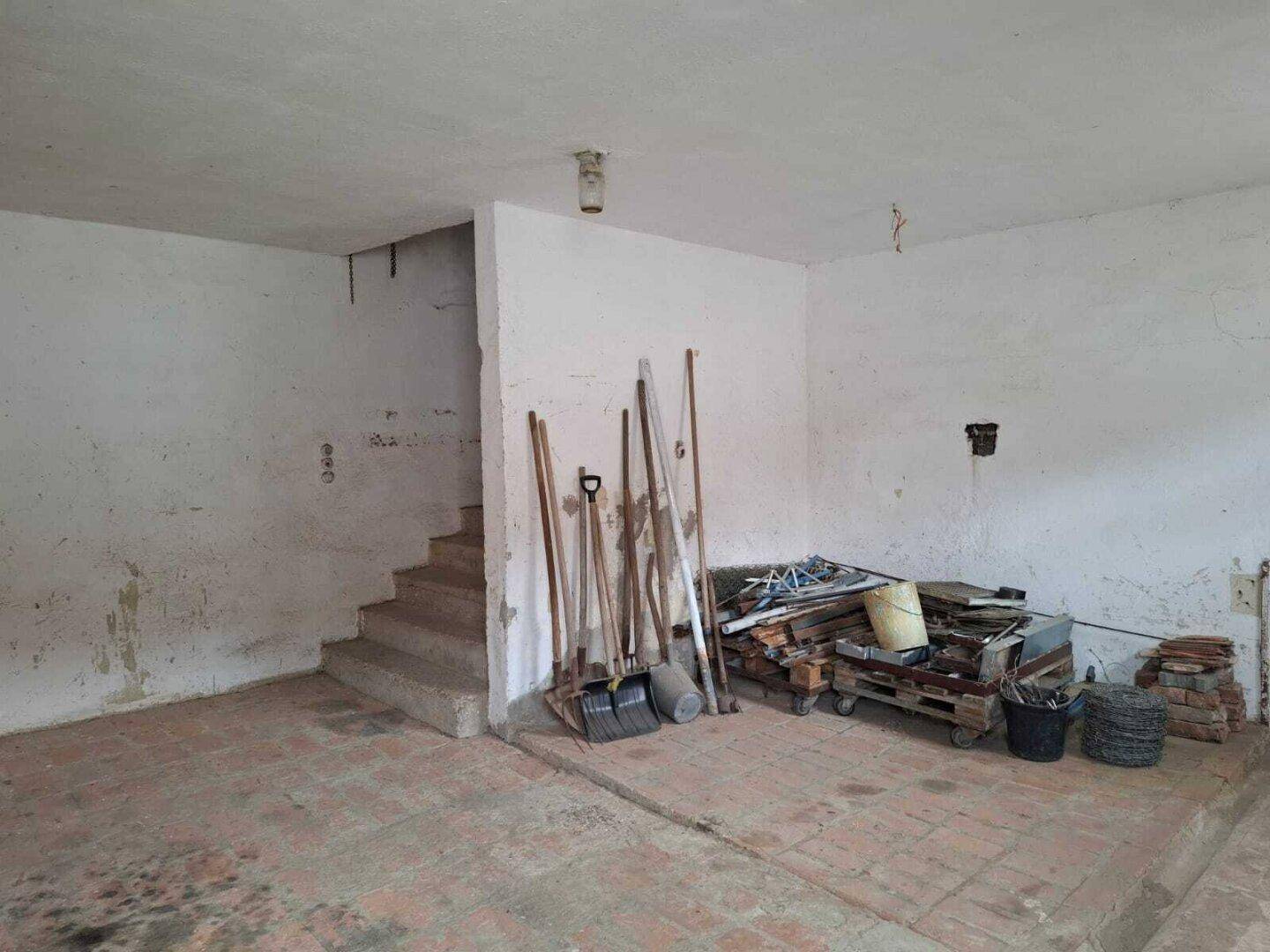 Kellerraum mit Betonboden, einer Treppe und verschiedenen Werkzeugen und Materialien gelagert.