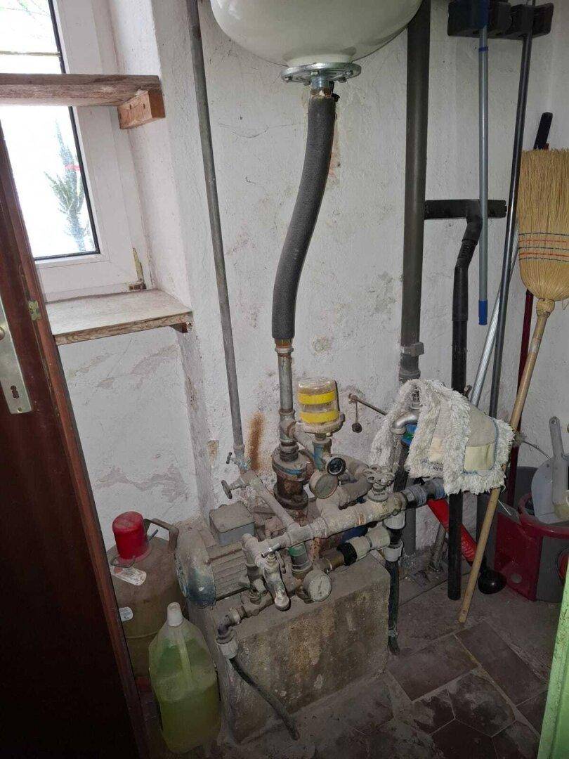 Technikraum mit Wasserpumpe, Rohren und einem kleinen Fenster, das Tageslicht hereinlässt.