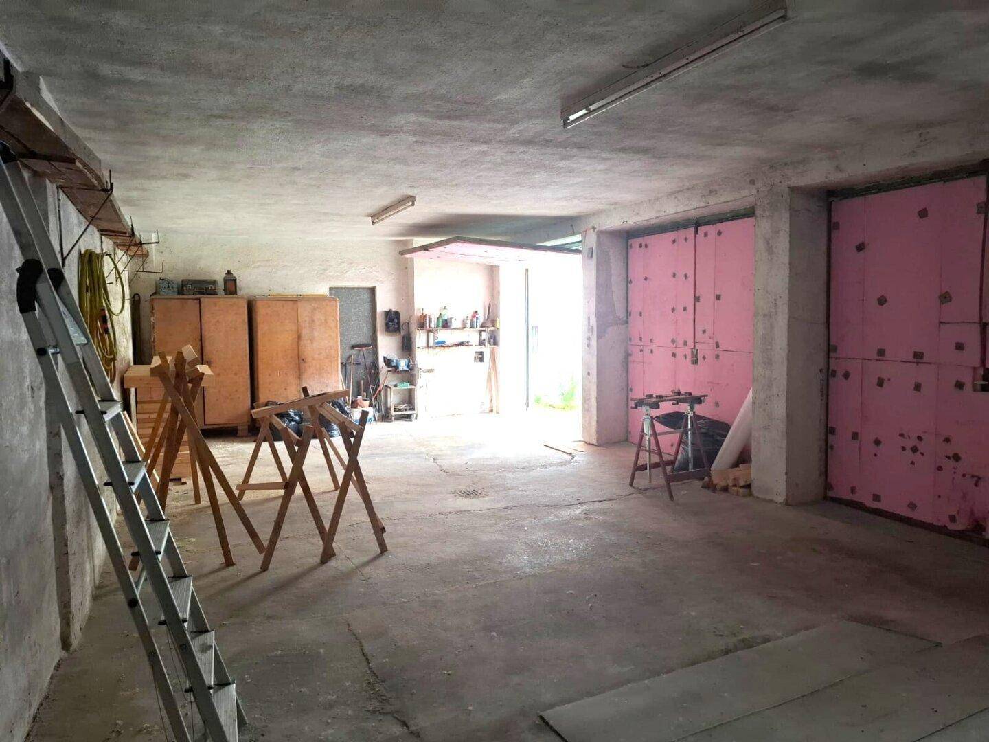 Große Garage oder Werkstatt mit Betonboden und rosa isolierten Toren, die viel Platz bietet.