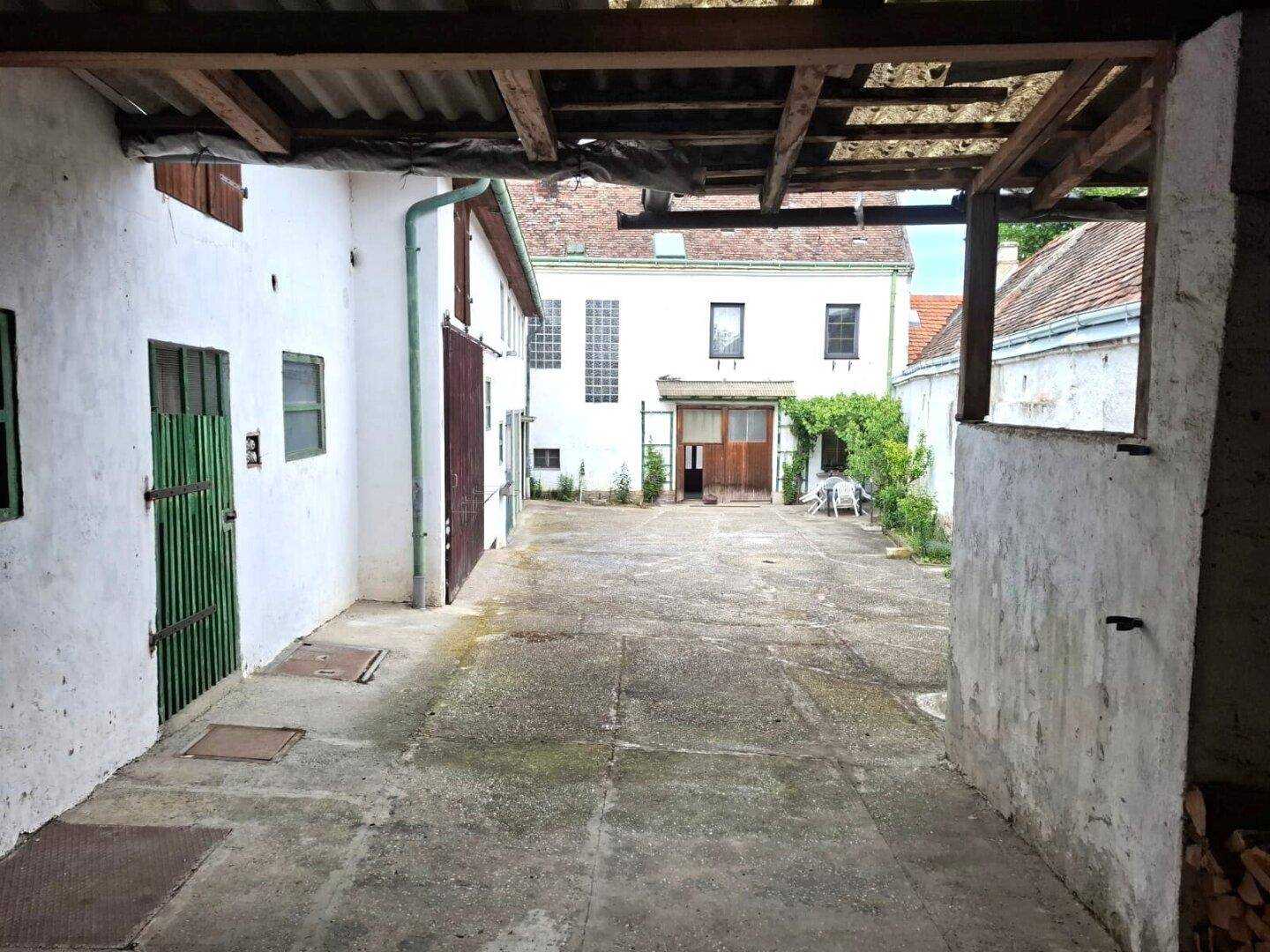 Innenhof zwischen alten Gebäuden mit Betonboden und rustikalen Holztüren.