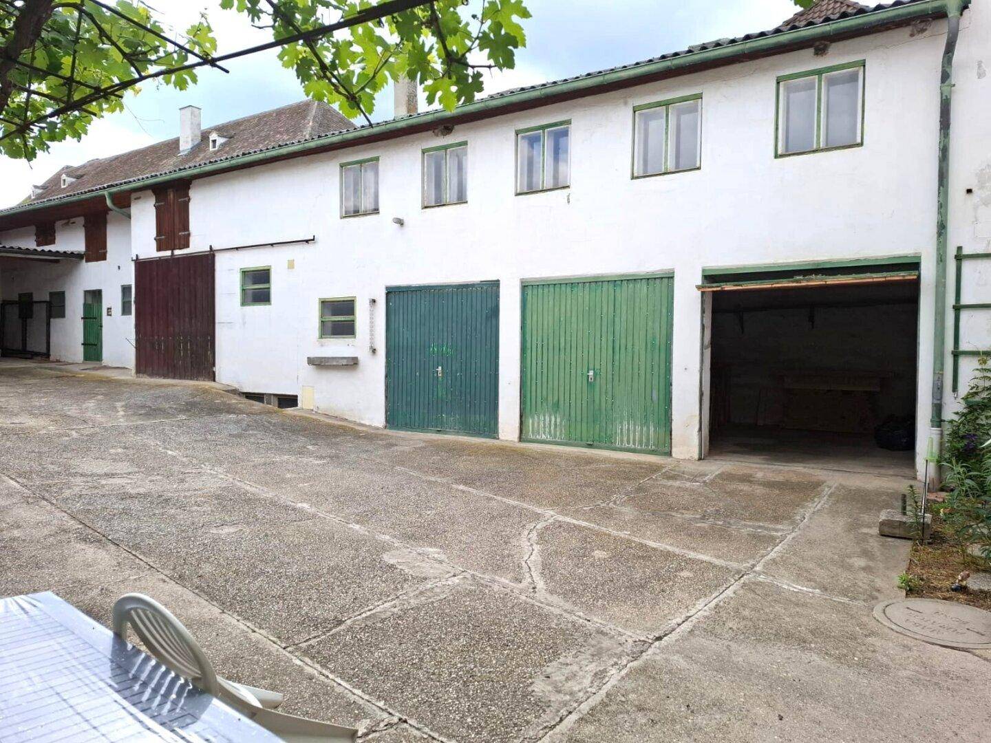 Langer weißer Gebäudeflügel mit mehreren grünen Garagentoren und Fenstern im Innenhof.
