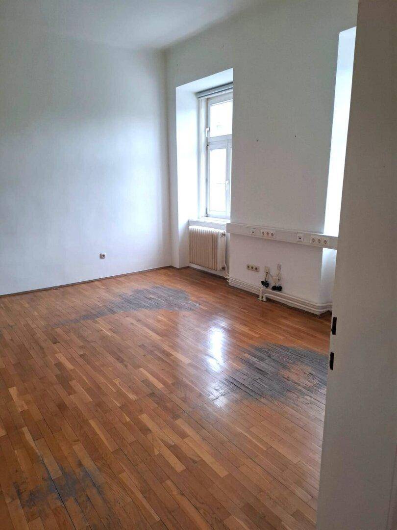 Leeres Zimmer mit Fischgrätparkettboden und sichtbaren Abnutzungsspuren, bereit für eine Renovierung.