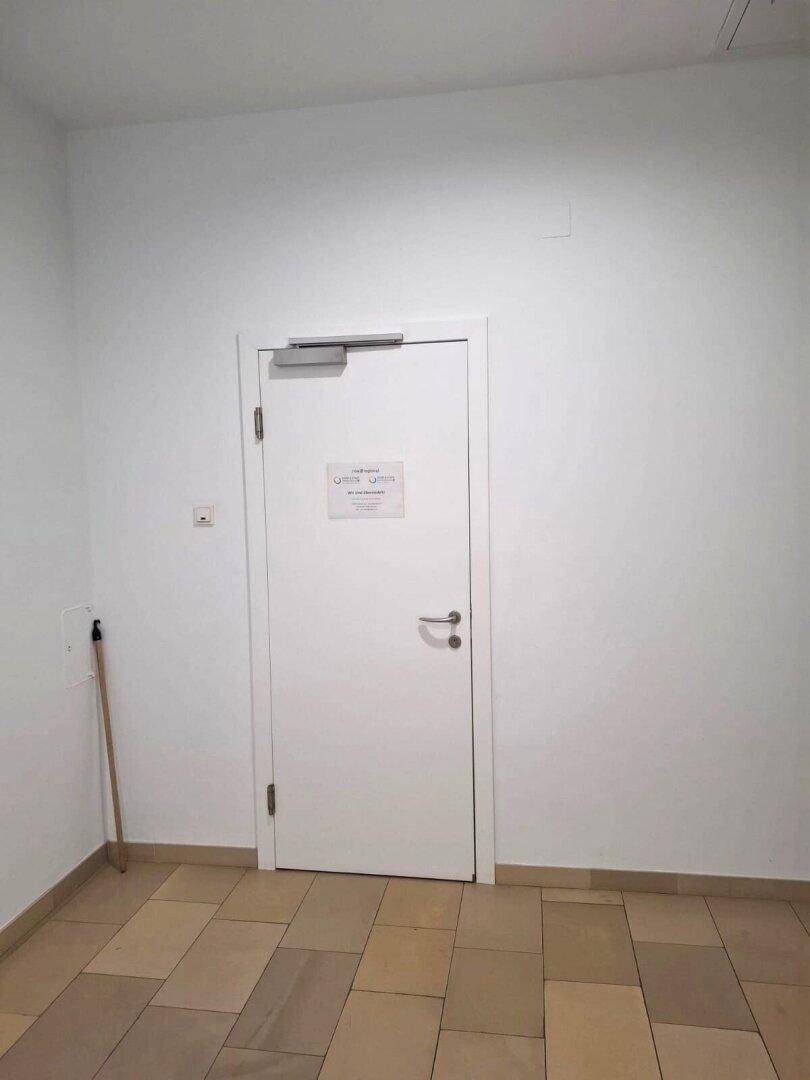 Heller Flur mit Fliesenboden und einer weißen Tür, die zu einem anderen Bereich führt.