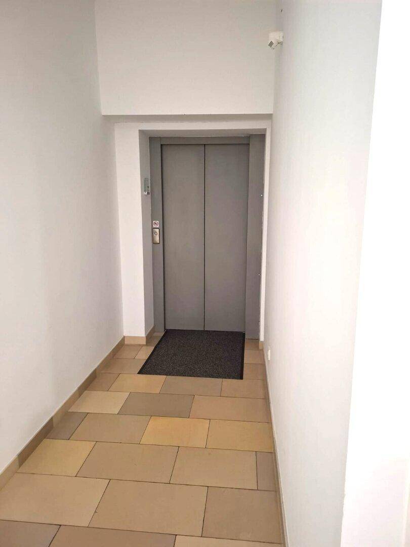 Heller Flur mit Fliesenboden und einem Aufzug, der Zugang zu den oberen Etagen des Gebäudes bietet.