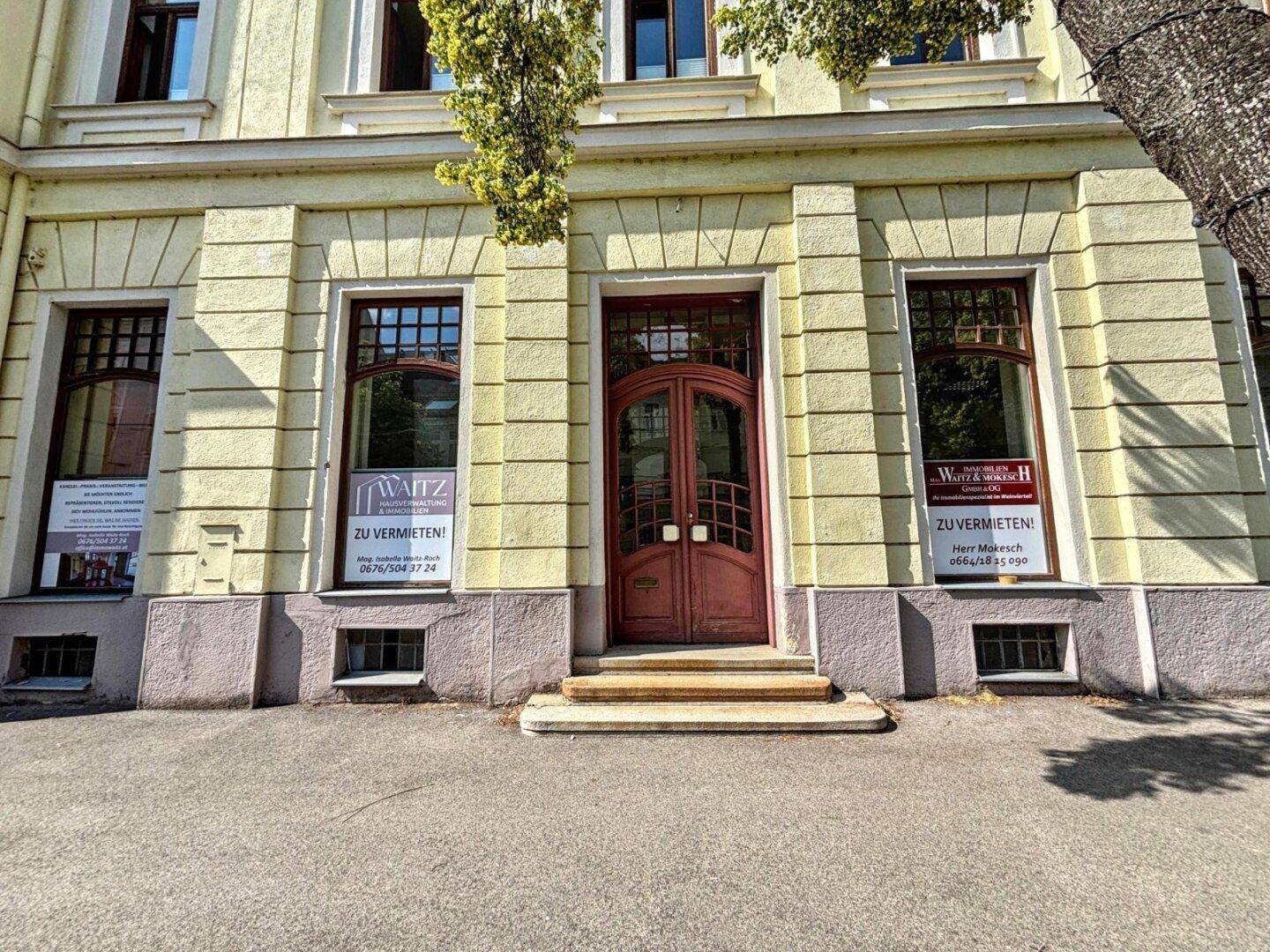 Detailansicht des Haupteingangs eines historischen Gebäudes mit Holztür und großen Fenstern.