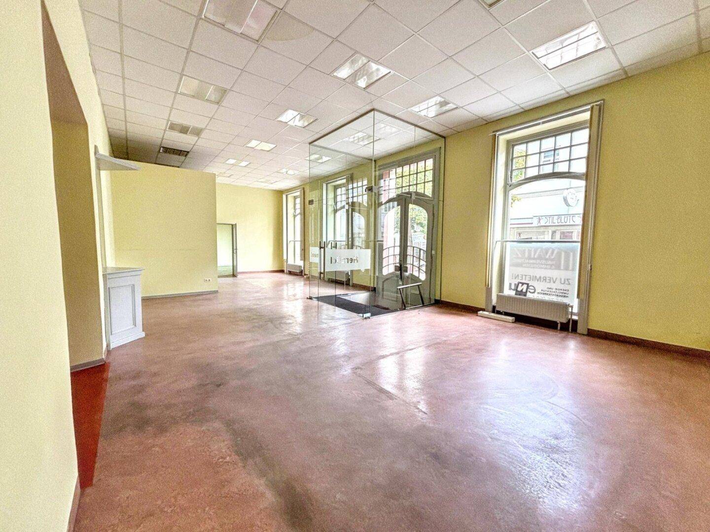 Geräumiger Gewerberaum mit hohen Decken, großen Fenstern und einem modernen Glasabtrennung.