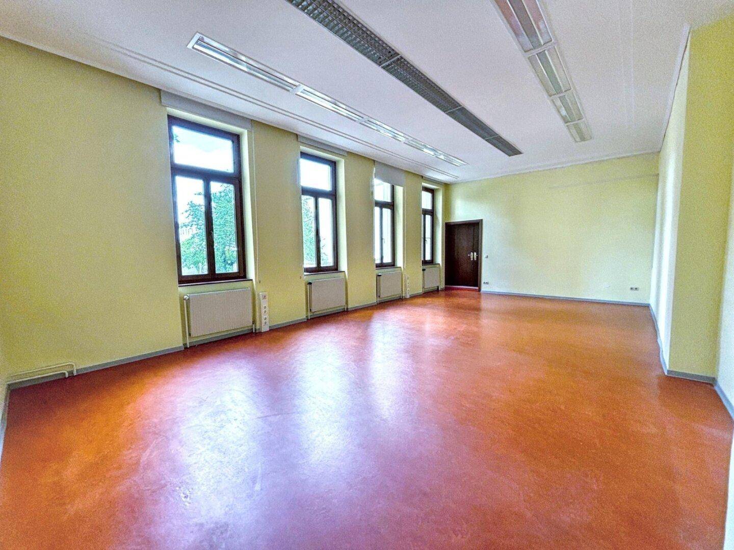 Heller Büroraum mit rotem Boden, gelben Wänden und einer Reihe von Fenstern.