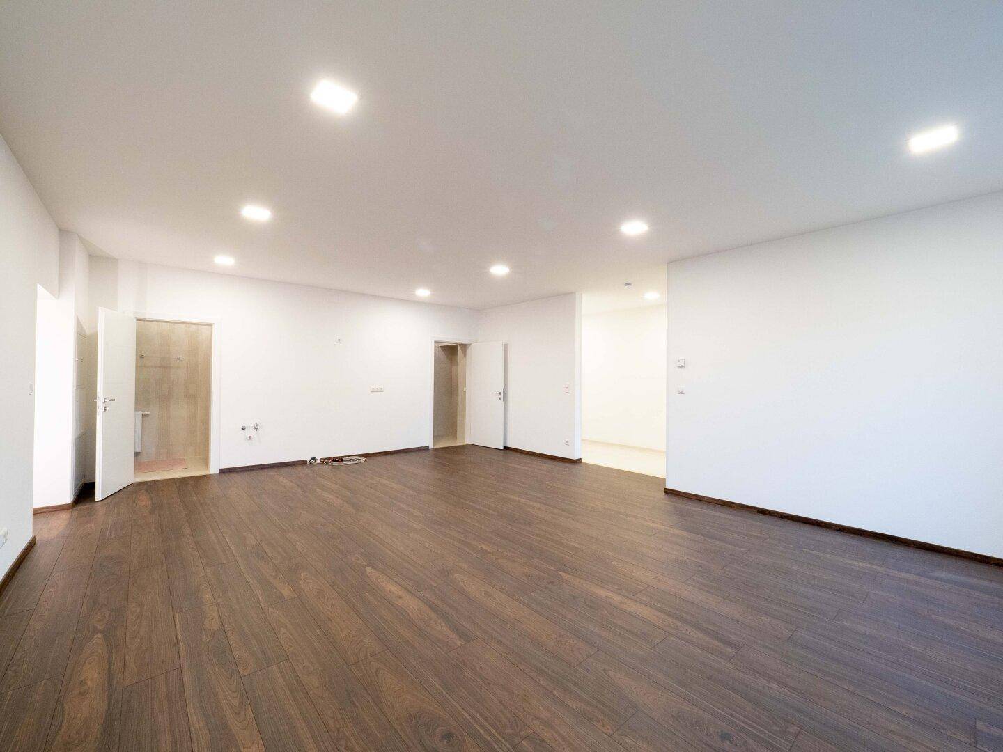 Weitläufiger Wohnbereich mit dunklem Holzboden und mehreren Türen, der vielseitige Einrichtungsmöglichkeiten bietet.