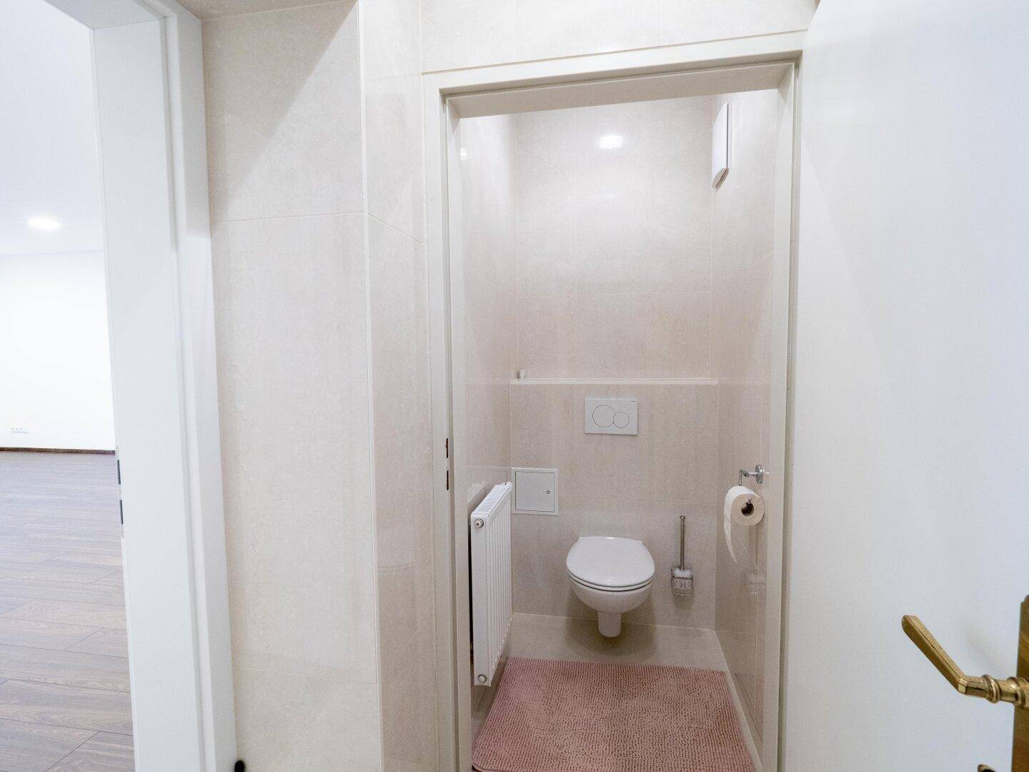 Separates Gäste-WC mit wandhängender Toilette und Heizkörper, ausgestattet mit hellen Fliesen.
