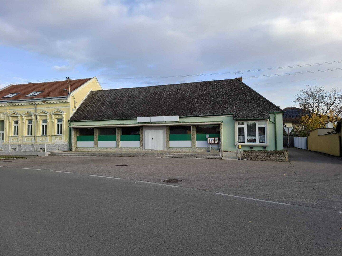 Gesamtansicht des Gebäudes mit Ladenfront und angrenzendem historischen Bauwerk in der Nachbarschaft.