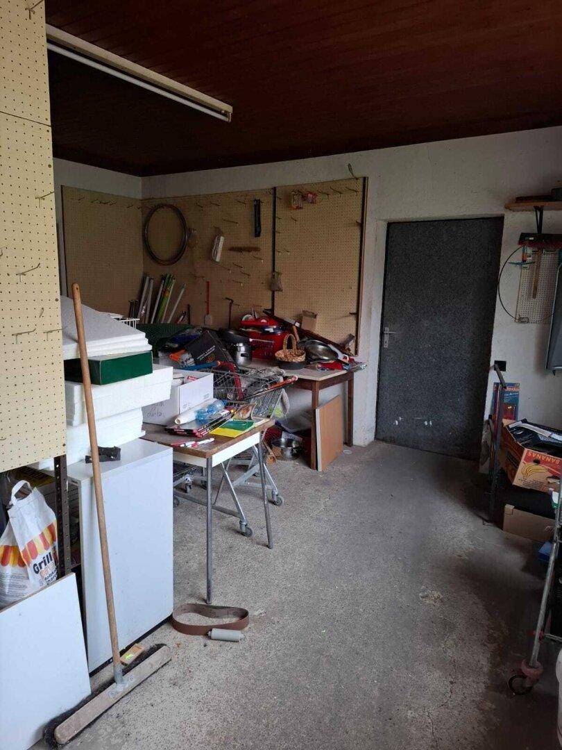 Abstellraum oder Werkstatt mit Betonboden und verschiedenen Gegenständen, die gelagert werden und Renovierung benötigen.