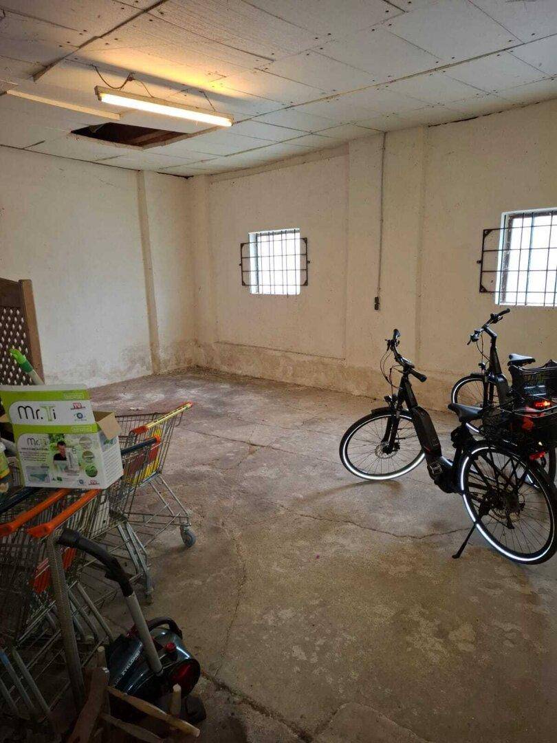 Geräumige Garage oder Lagerfläche mit Betonboden und Fenstern mit Gitterstäben, die aufgeräumt werden muss.