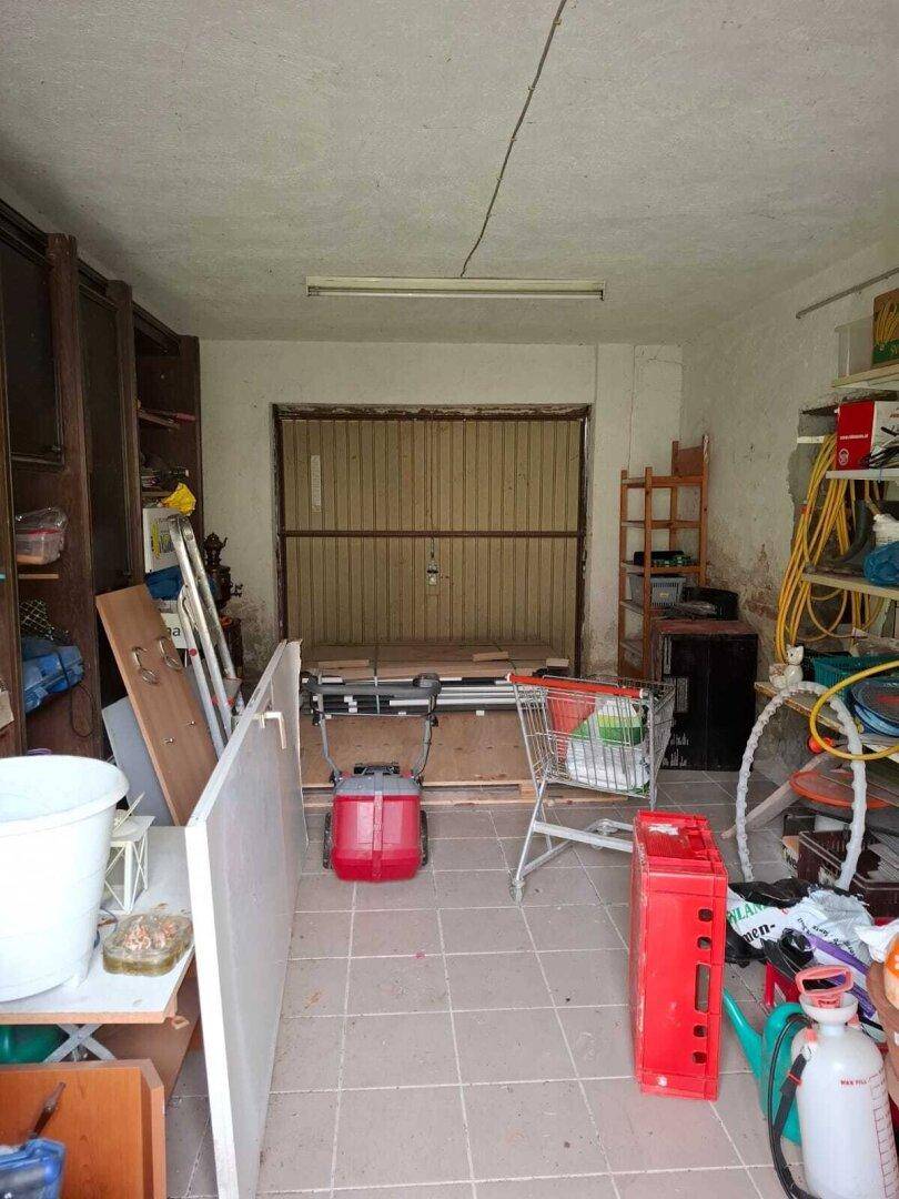 Lagerraum mit Regalen und Fliesenboden, der eine breite Öffnung zur Außenseite hat und Renovierung benötigt.