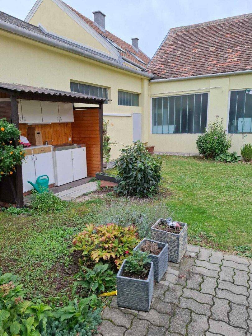 Gartenbereich mit Hochbeeten, Rasenfläche und einer kleinen Außenküche für gesellige Abende.