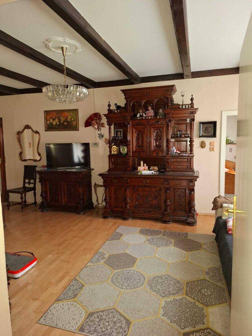 Wohnzimmer mit Holzbalkendecke, Parkettboden und einem großen, antiken Schrank als Blickfang.