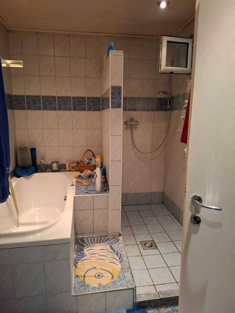Badezimmer mit Badewanne, Dusche und Fliesen in Blautönen, das eine Renovierung benötigt und älter ist.